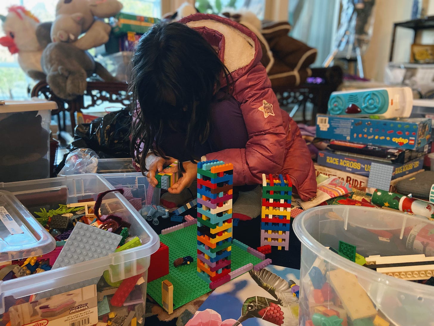 Girl with head down playing Legos, surrounded by toys