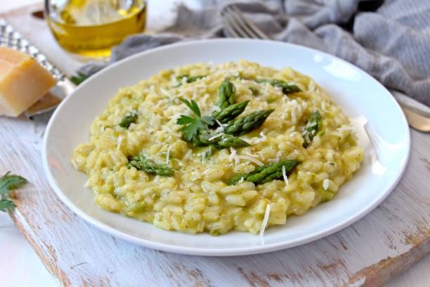 Italian risotto with spring asparagus and parmesan cheese in plate on light background. Top view with copy space. risotto stock pictures, royalty-free photos & images
