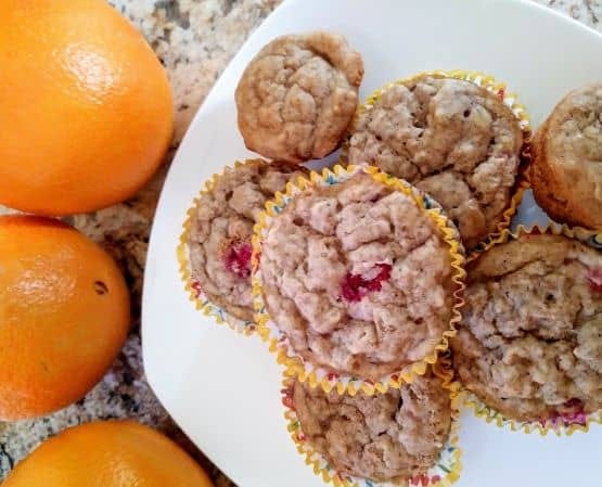Cranberry orange oatmeal muffins on white plate next to oranges