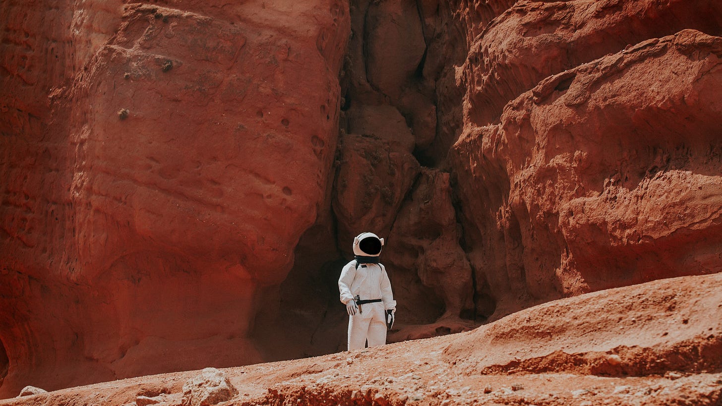 photography of astronaut standing beside rock formation during daytime photo