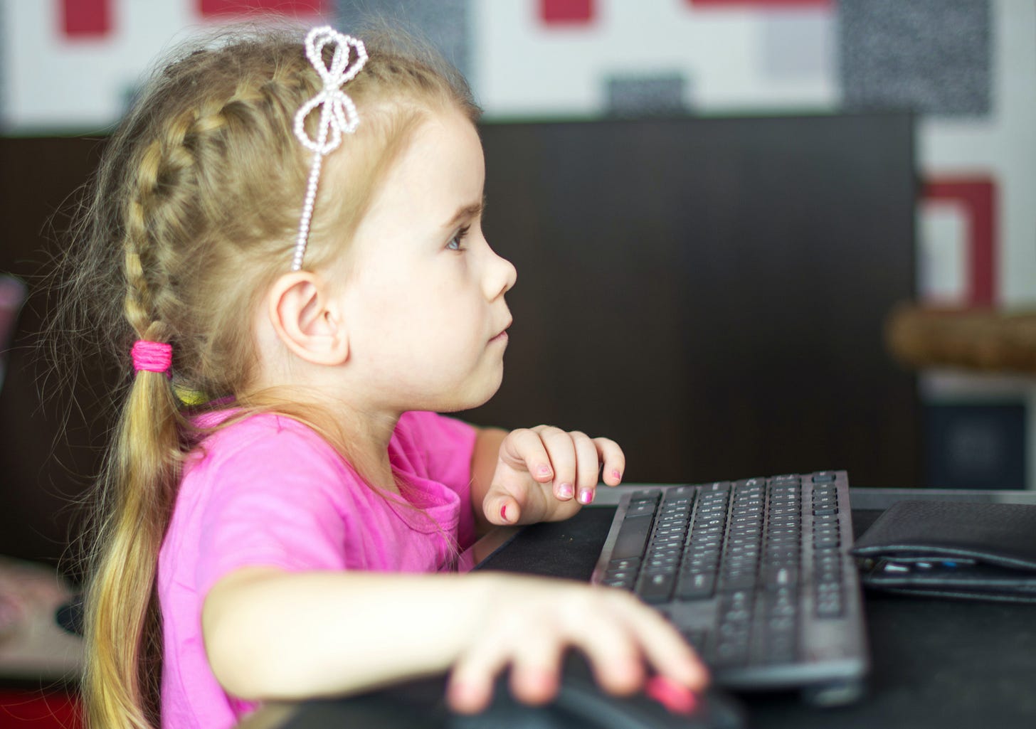 5 yr old girl working at school on computer dressed in pretty pink