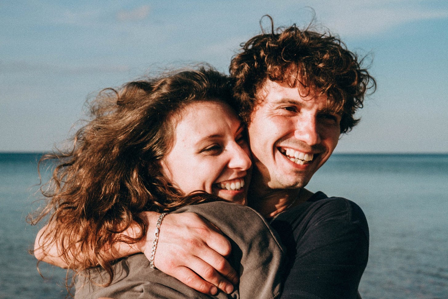 A smiling couple embraces on a beach.