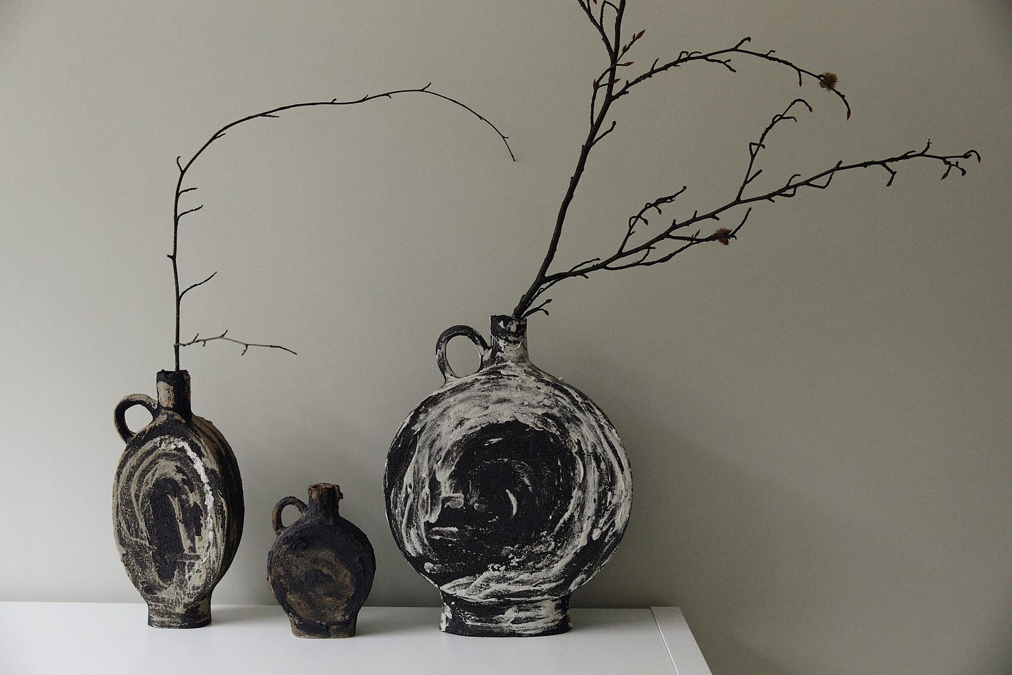 Three vessels on a tabletop with bare winter branches