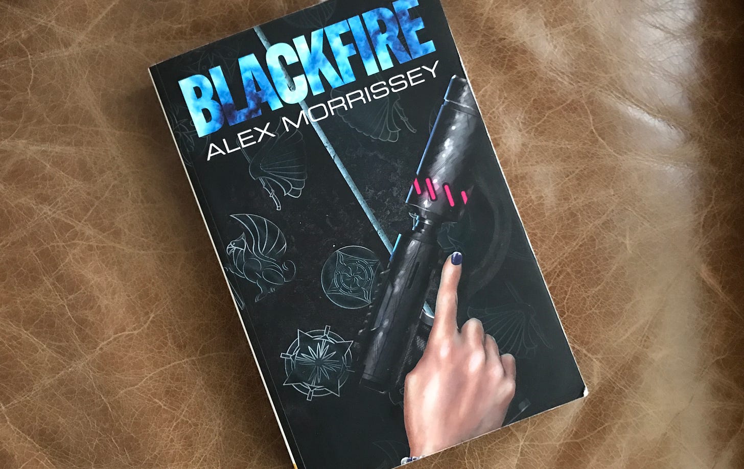 Image of the book Blackfire, by Alex Morrissey laying on a leather armchair cushion.