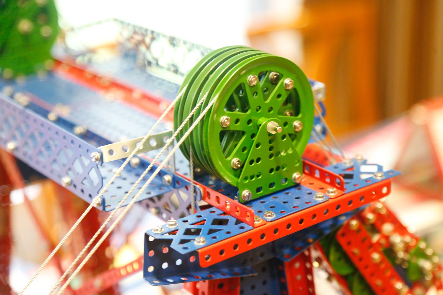 Close-up of a portion of a colorful erector set, featuring a set of green pulleys side by side with cables running through them