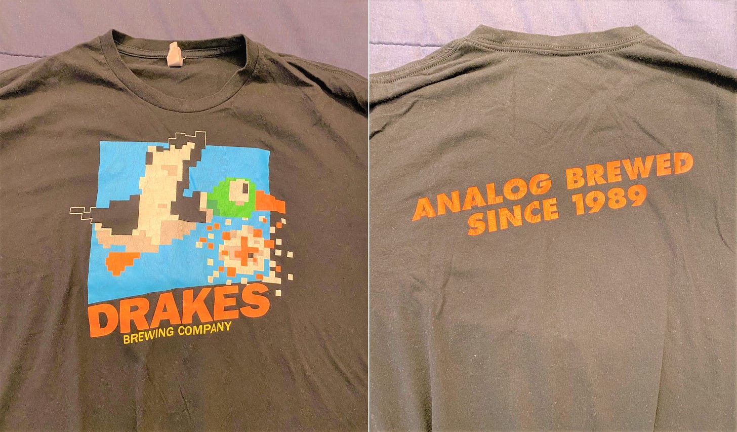 A t-shirt with an 8-bit duck and Drake's Brewing Company on the front, and the slogan "Analog Brewed since 1989" on the back
