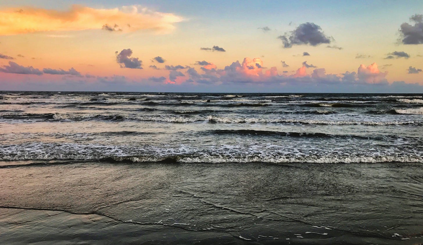 The waves rolling onto the shore with a sky of blue and orange, peach and grey clouds meeting the horizon