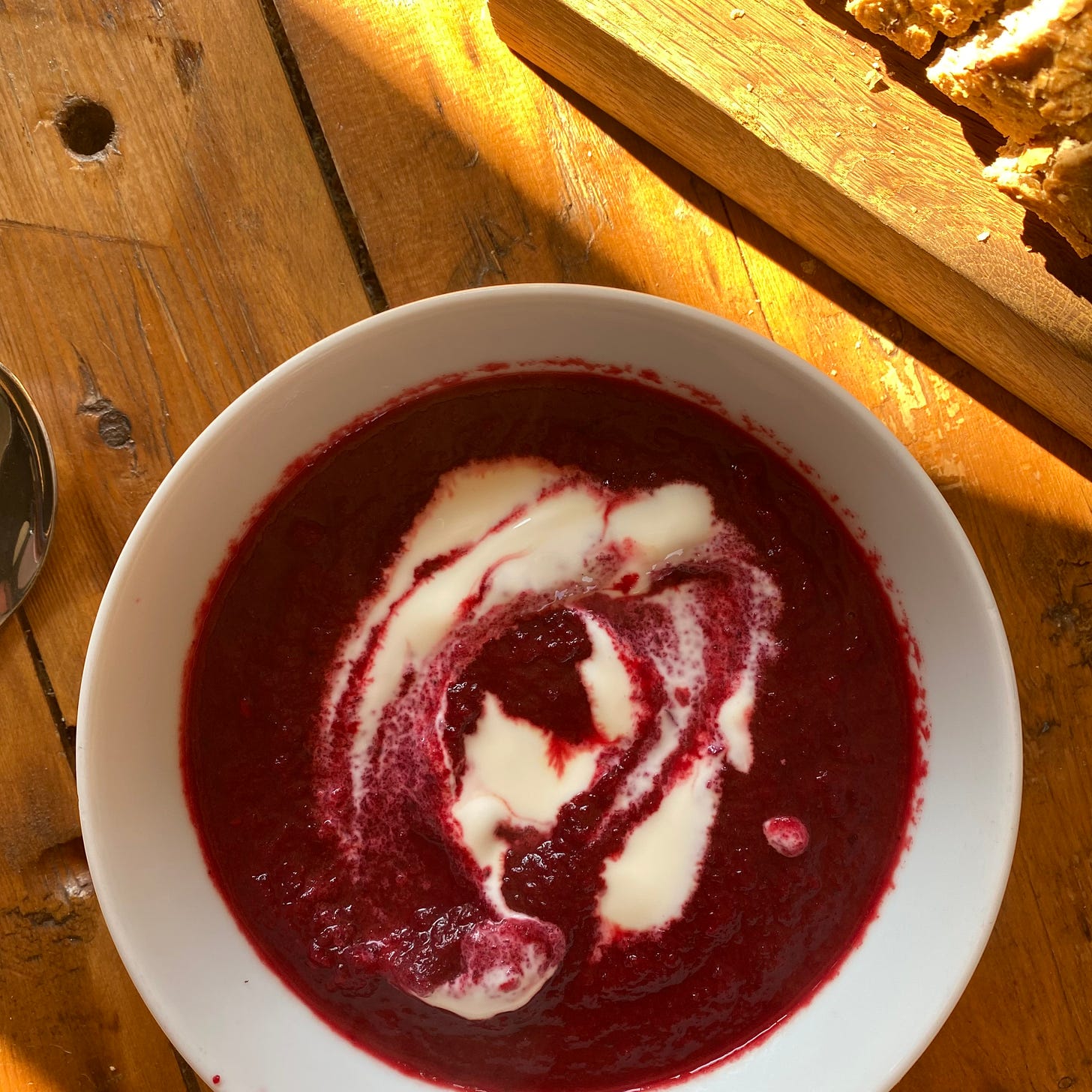 Bowl full of beetroot soup with a swirl of yoghurt. Chopping board with crusty bread to the top right.