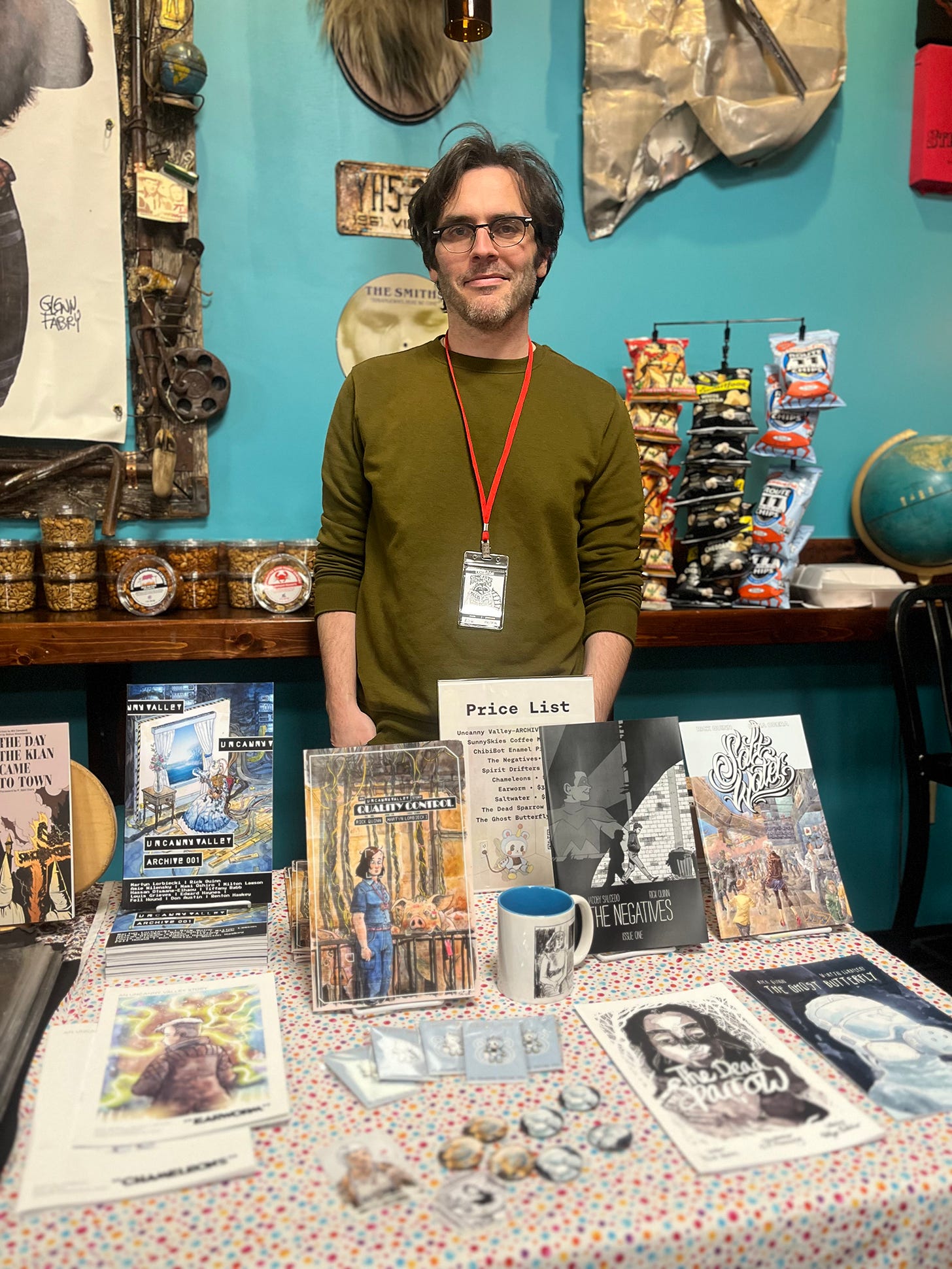 A gray-haired writer of things standing behind a table full of his self-published works.