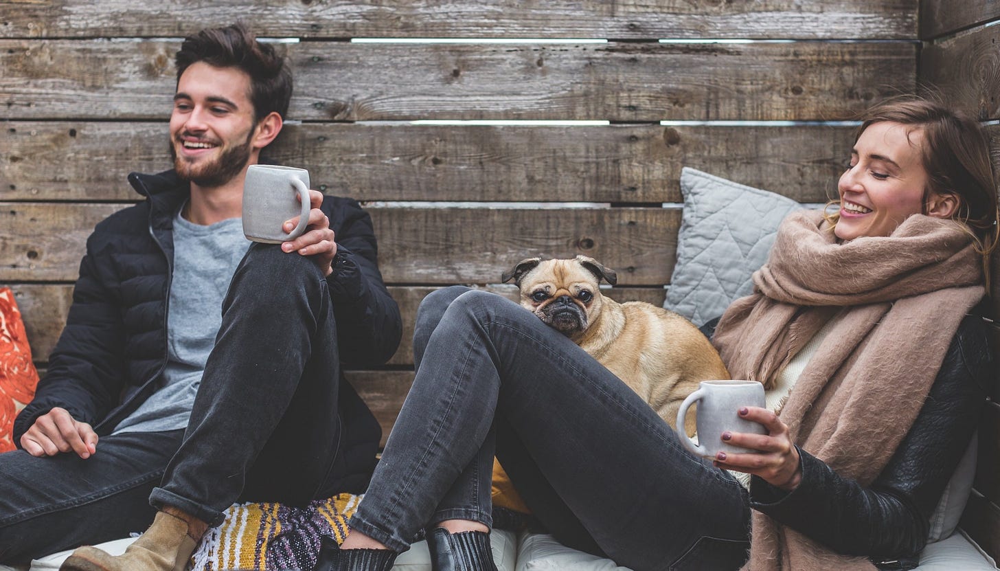 A couple holding coffee mugs with a pet pug