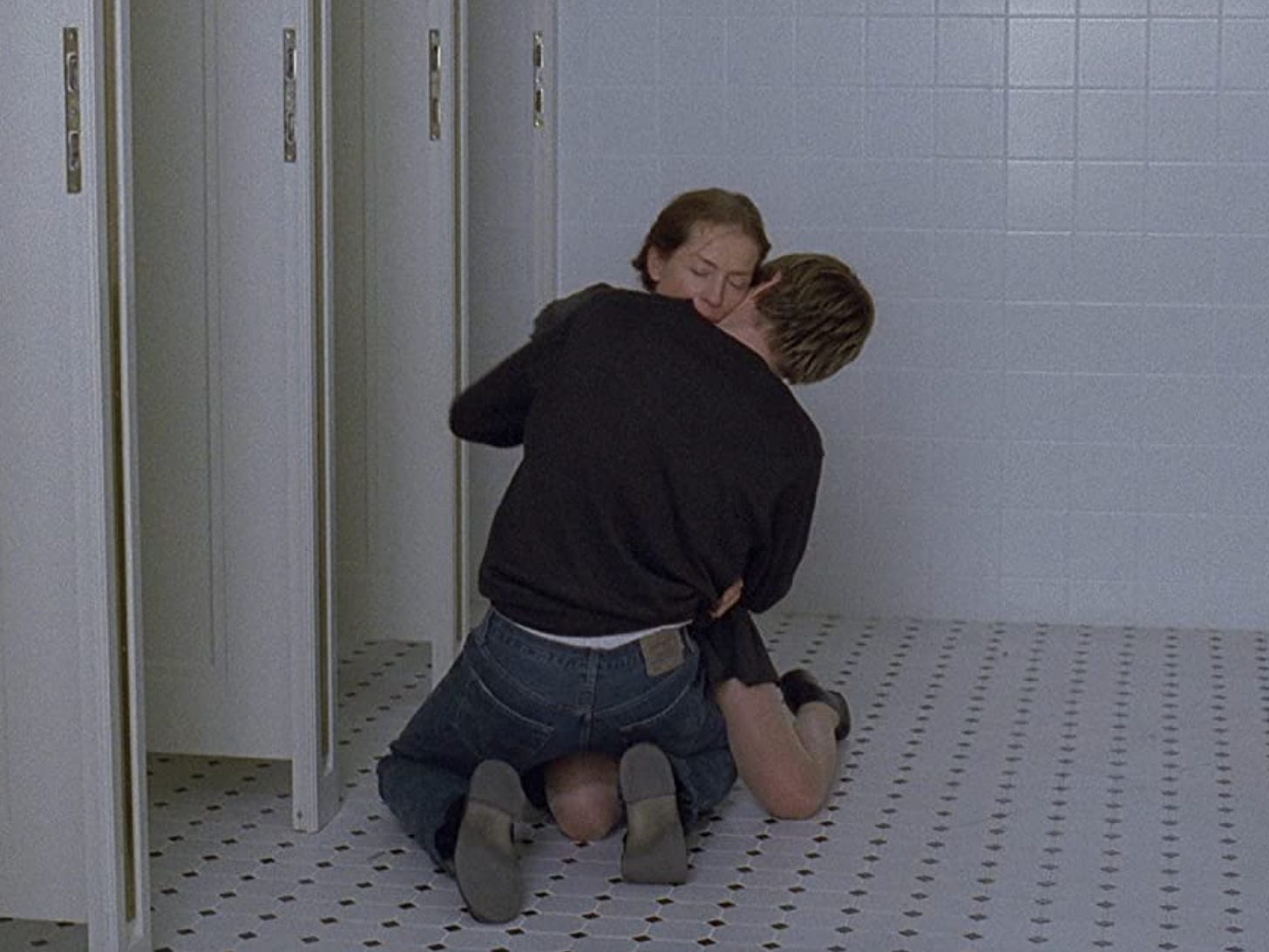 Isabelle Huppert embracing Benoit Magimel in a white-tiled bathroom.