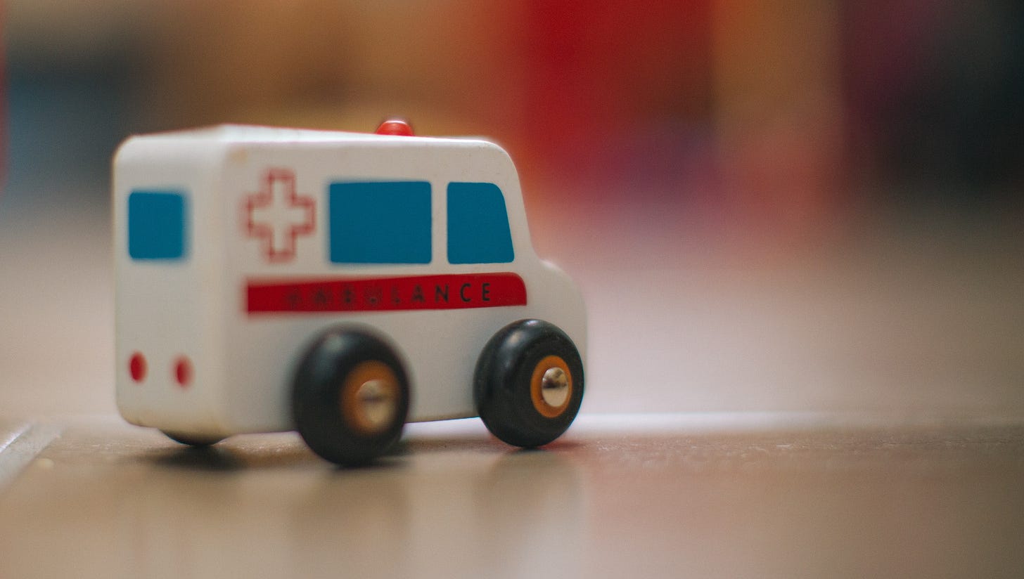 Closeup photograph of a tiny toy ambulance on slightly reflective floor, background out of focus