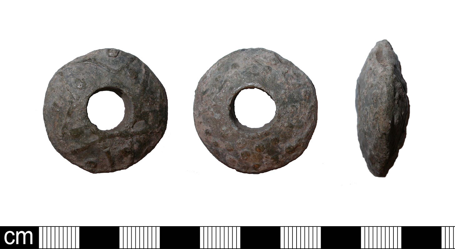 image of a roman spindle whorl made from metal. the spindle whorls is circular with a whole in the middle, like a doughnut, and about 3cm in diameter. there is an above, below and side shot. the spindle whorl is decorated with some sort of geometric design.