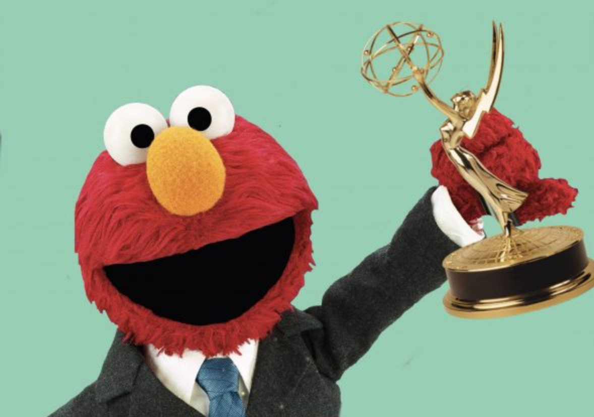 Elmo in a suit holding up an Emmy award