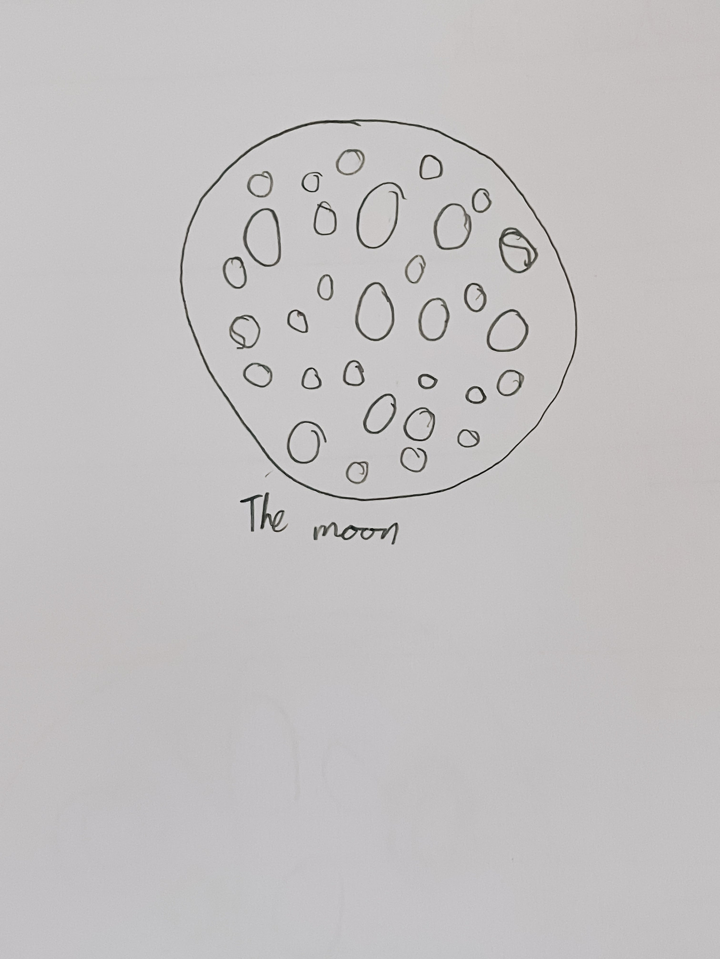 A child's pencil drawing of the moon with the caption "the moon" written underneath.