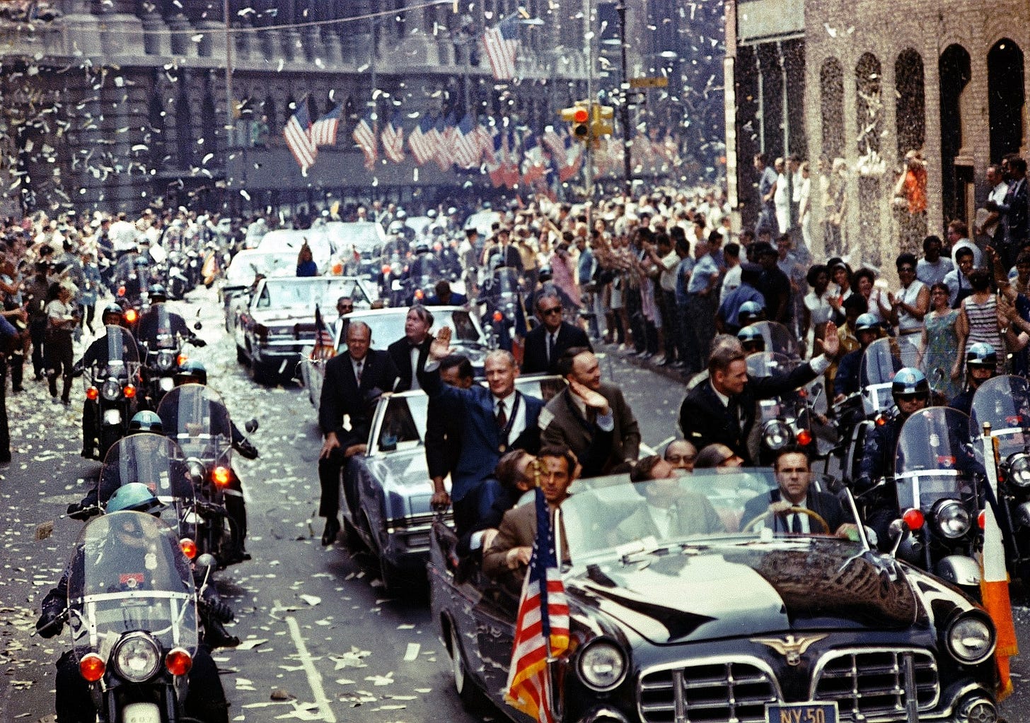 Neil Armstrong waving from a convertible in a confetti-strewn ticker tape parade proceeding down a New York City street.