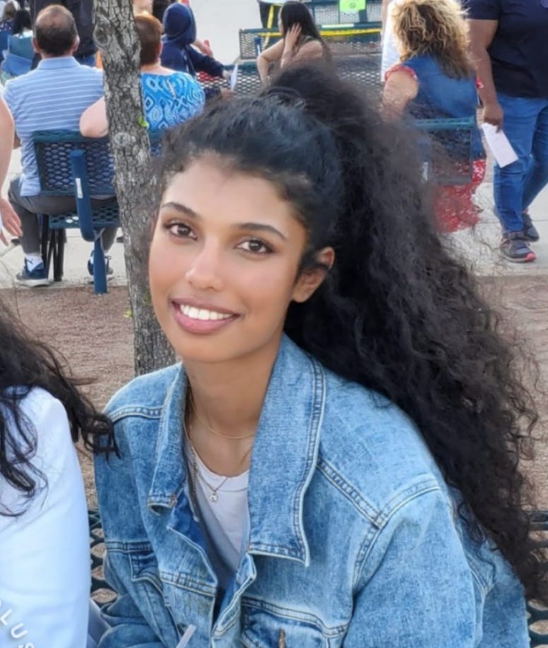 Aina Marzia, a 16-year-old Pakistani girl in a big jean jacket smiles at the camera. She has long curly hair.