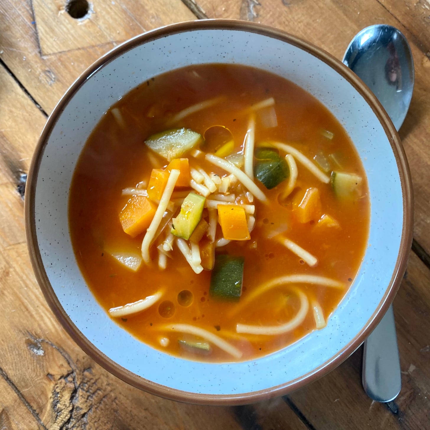 Bowl of minestrone soup with courgette, carrot, tomato and pasta, with a spoon to one side