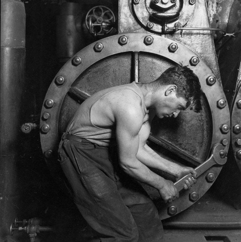 A black and white picture of a muscular white man operating some kind of machinery. He concentrates hard on his work