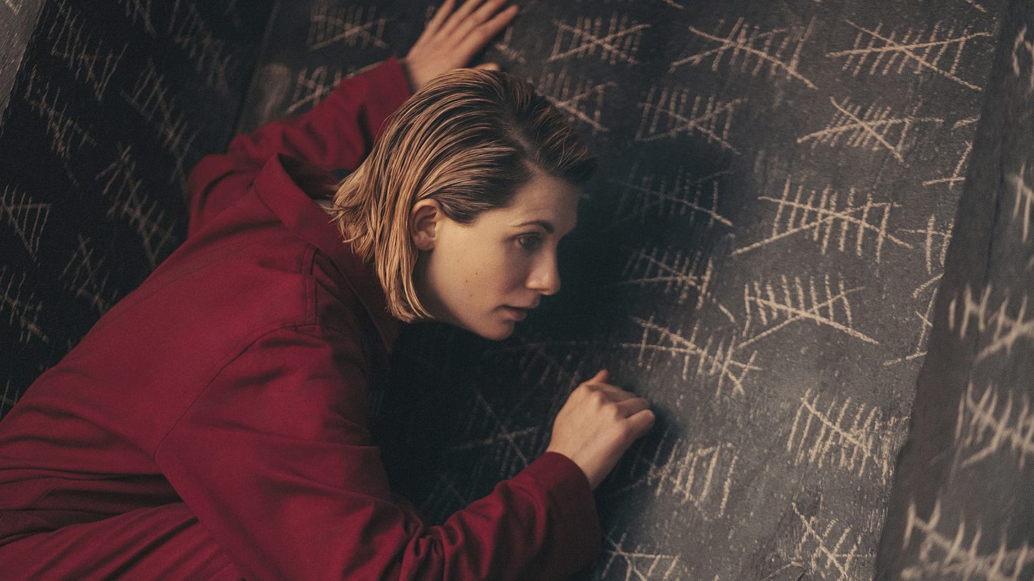 This image shows the Thirteenth Doctor (played by Jodie Whittaker) dressed in a red Judoon-prison jumpsuit as she knocks on the wall of her jail cell. This wall is covered with hashes, each of which marks another day's passing. This image shows the Thirteenth Doctor (played by Jodie Whittaker) dressed in a red Judoon-prison jumpsuit as she knocks on the wall of her jail cell. This wall is covered with hashes, each of which marks another day's passing.