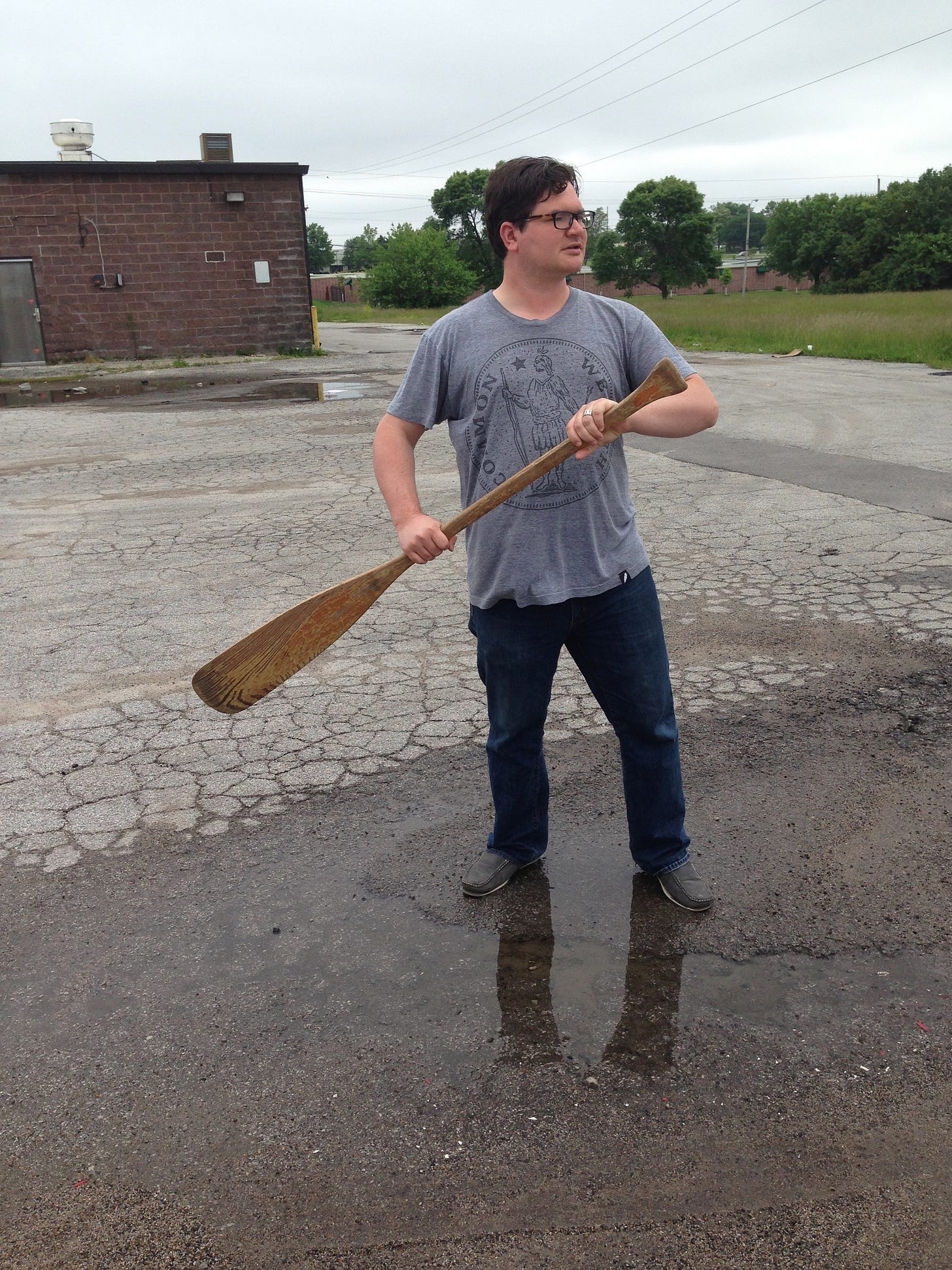 A thirtysomething white male stands in a puddle holding an oar
