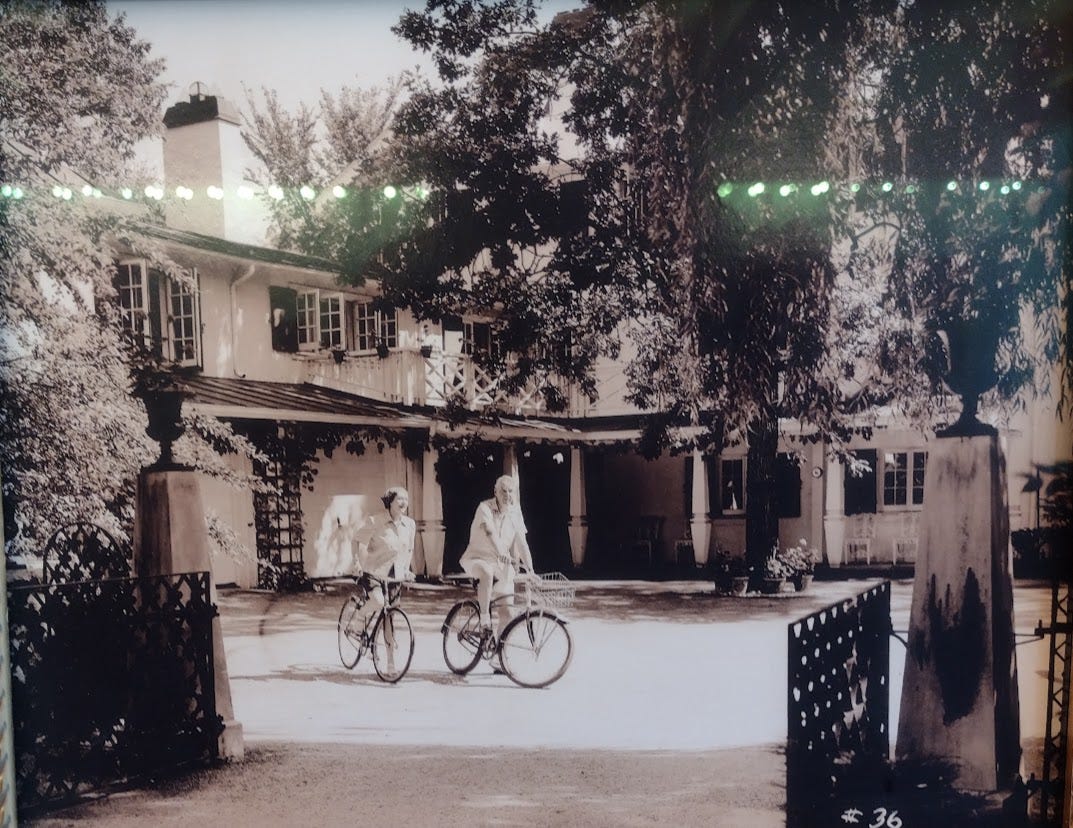 Man and woman on bicycles outside same house as above Man and woman on bicycles outside same house as above