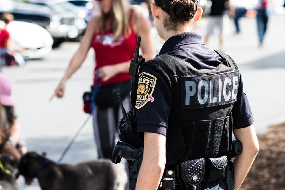police woman standing near black dog in front of woman wearing red top