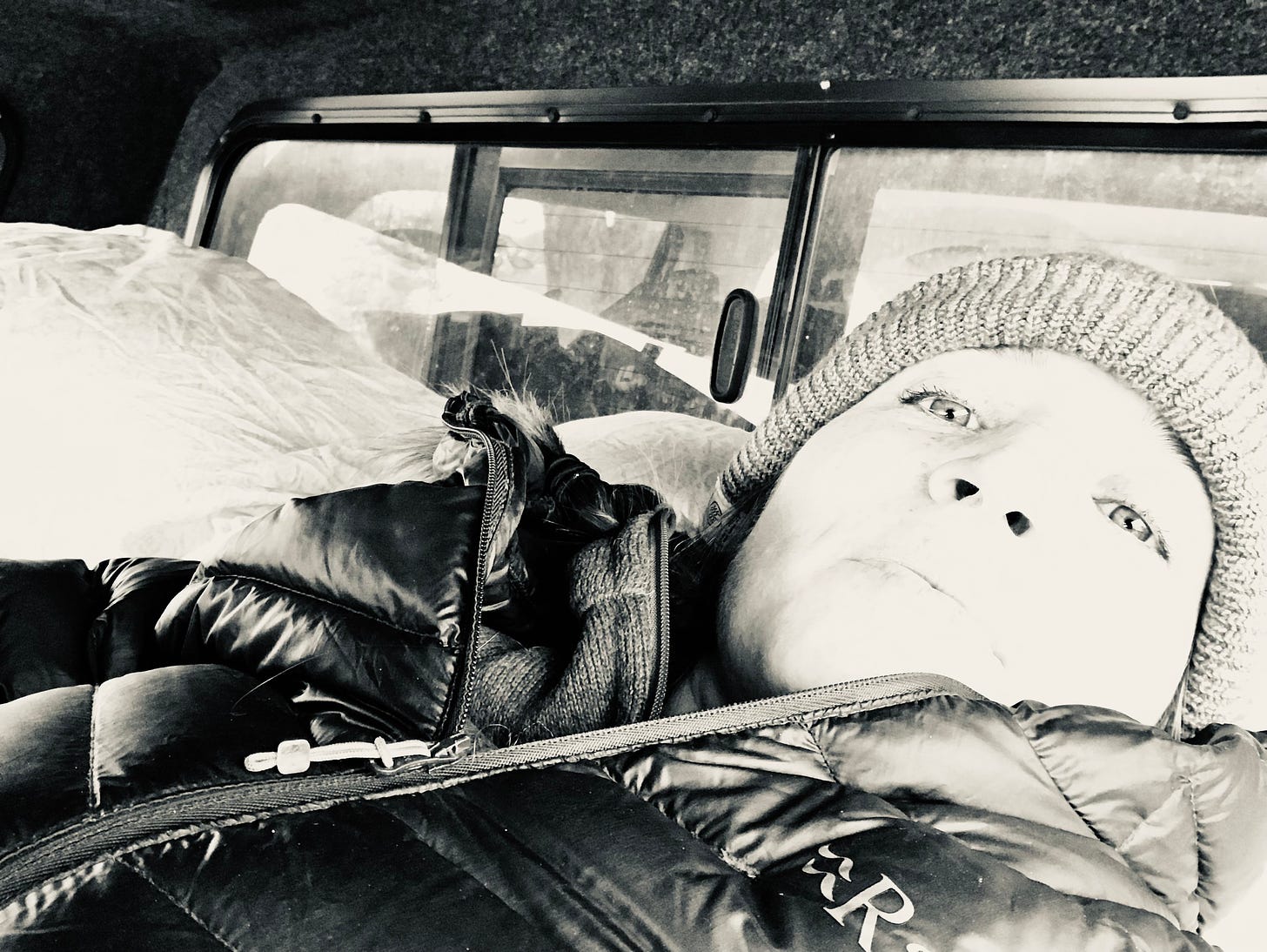 black and white photo of the author wearing a winter hat and coat, lying down in the back of the truck