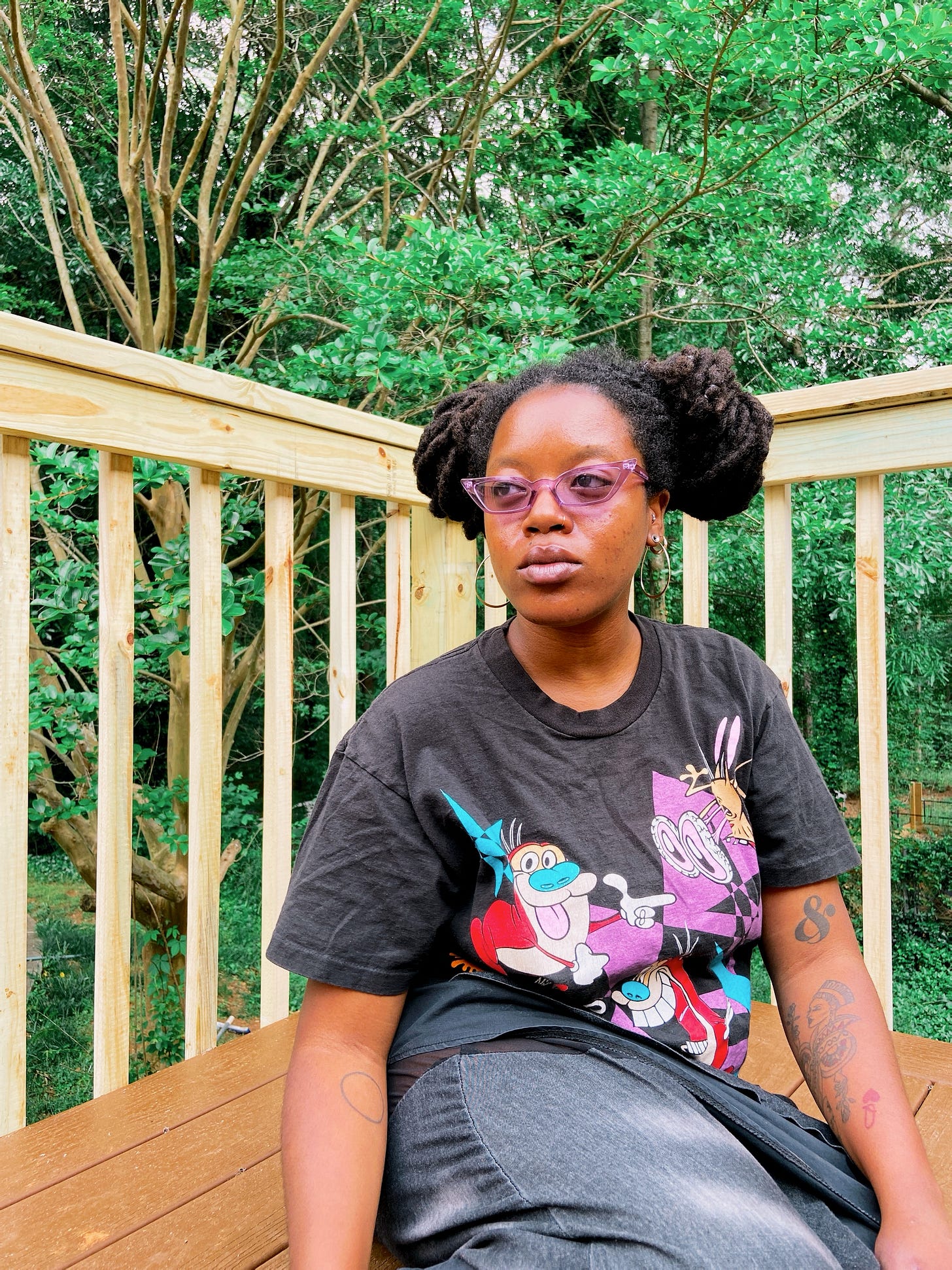 Tay wearing the aforementioned Ren & Stimpy tee while sitting outside on a wooden deck in front of lush green trees.