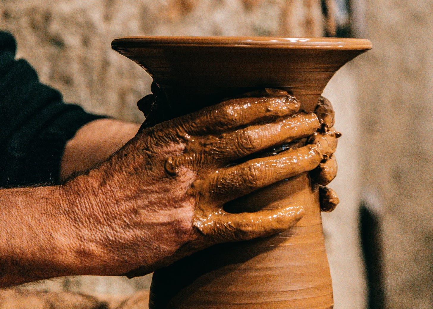 Man with hands in clay making vase on pottery wheel