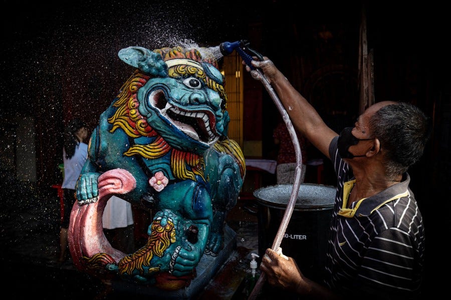 A person uses a hose to spray water on a colorful religious statue.