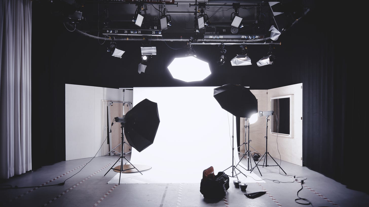 a studio is set up with bright lights shining down onto a white sheet backdrop. Behind the setup are black curtains.