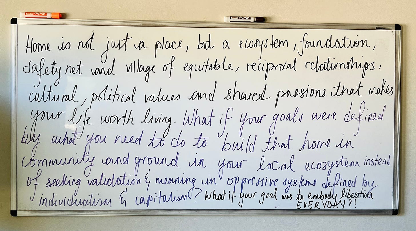 A whiteboard on which Ayesha has written in cursive: “Home is not just a place, but an ecosystem, a foundation, safety net and a village of equitable, reciprocal relationships, cultural, political values and shared passions that makes your life worth living. What if your goals were defined by what you need to do to build that home in community and ground in your local ecosystem instead of seeking validation & meaning in oppressive system defined by individualism & capitalism? What if your goal was to embody liberation EVERYDAY?”