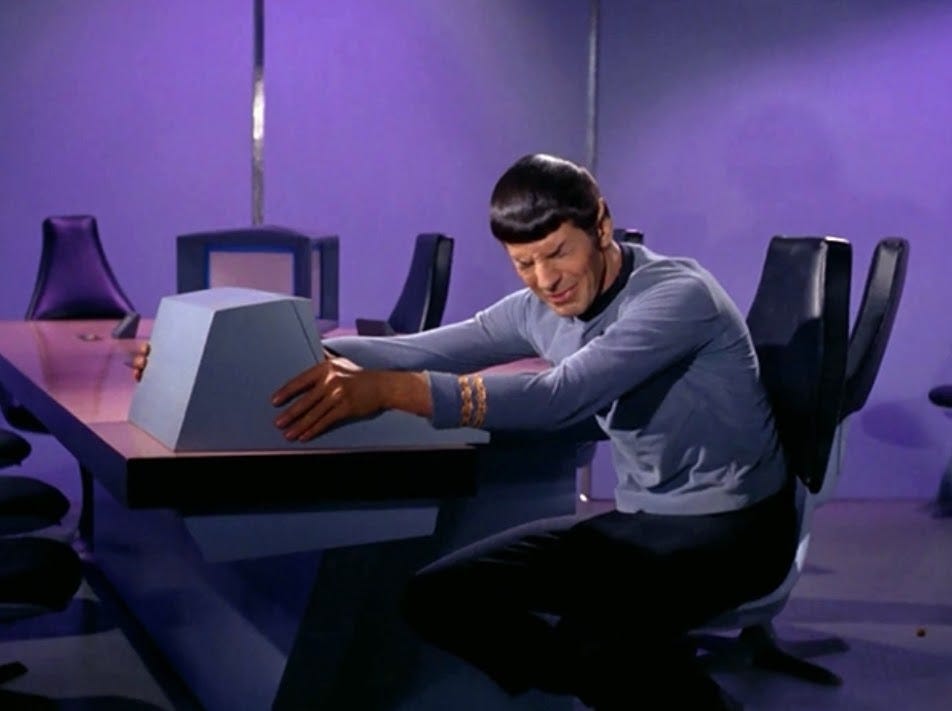 Spock is sitting at a conference table. He's ugly face crying while facing a computer and holding onto it with his hands.