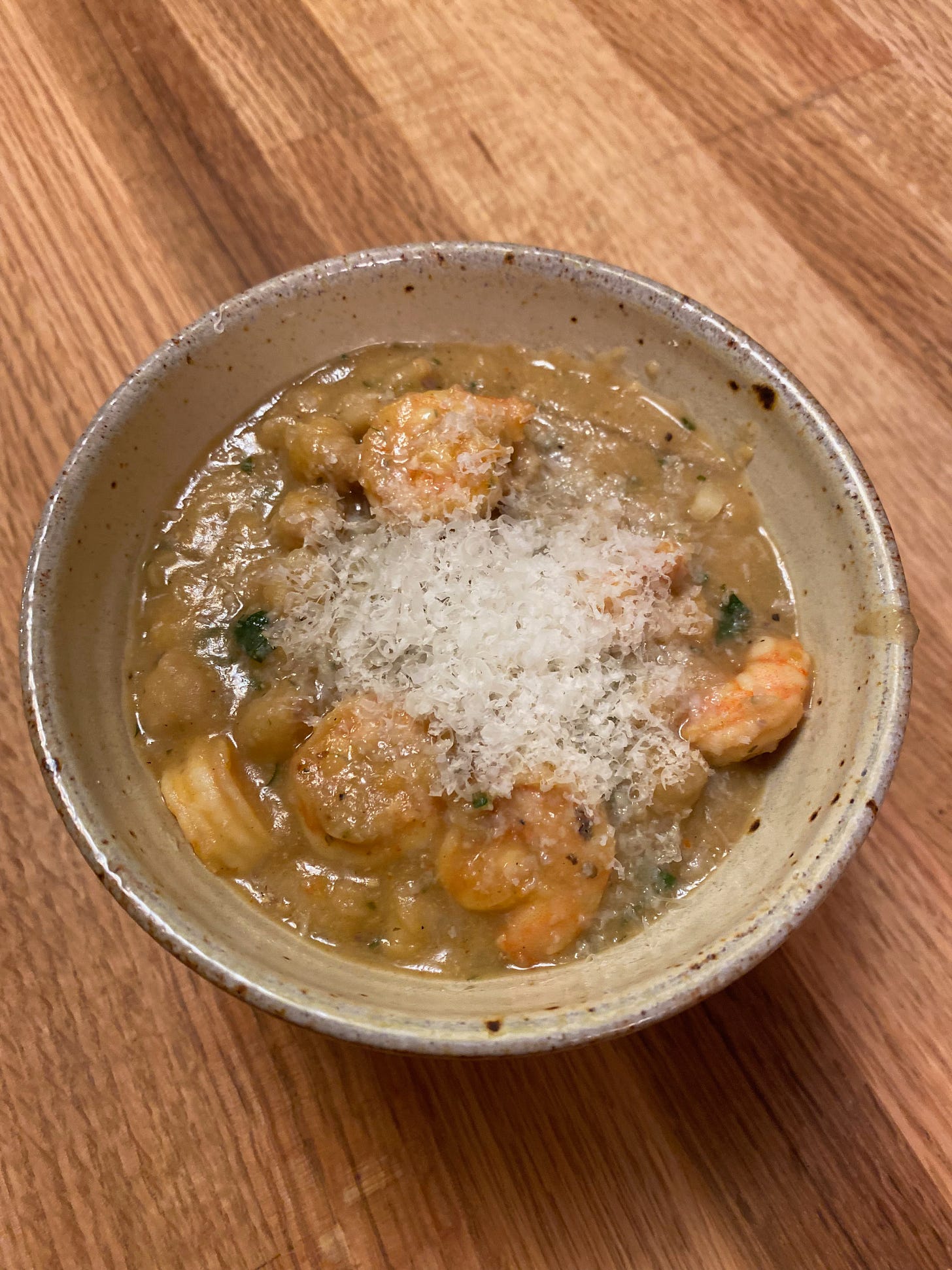 A bowl of thick chickpea stew, full of small shrimp and flecks of parsley, topped with a large pile of grated Parmesan.