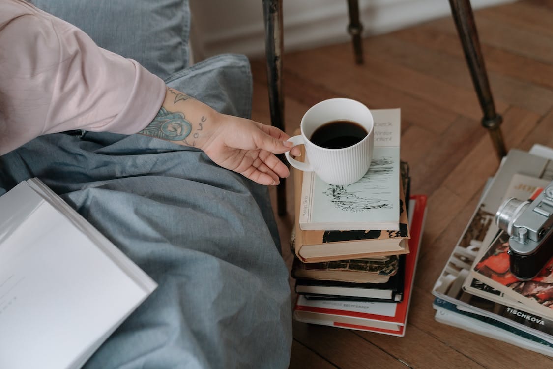 Free Hand taking a cup of coffee from the pile of books Stock Photo