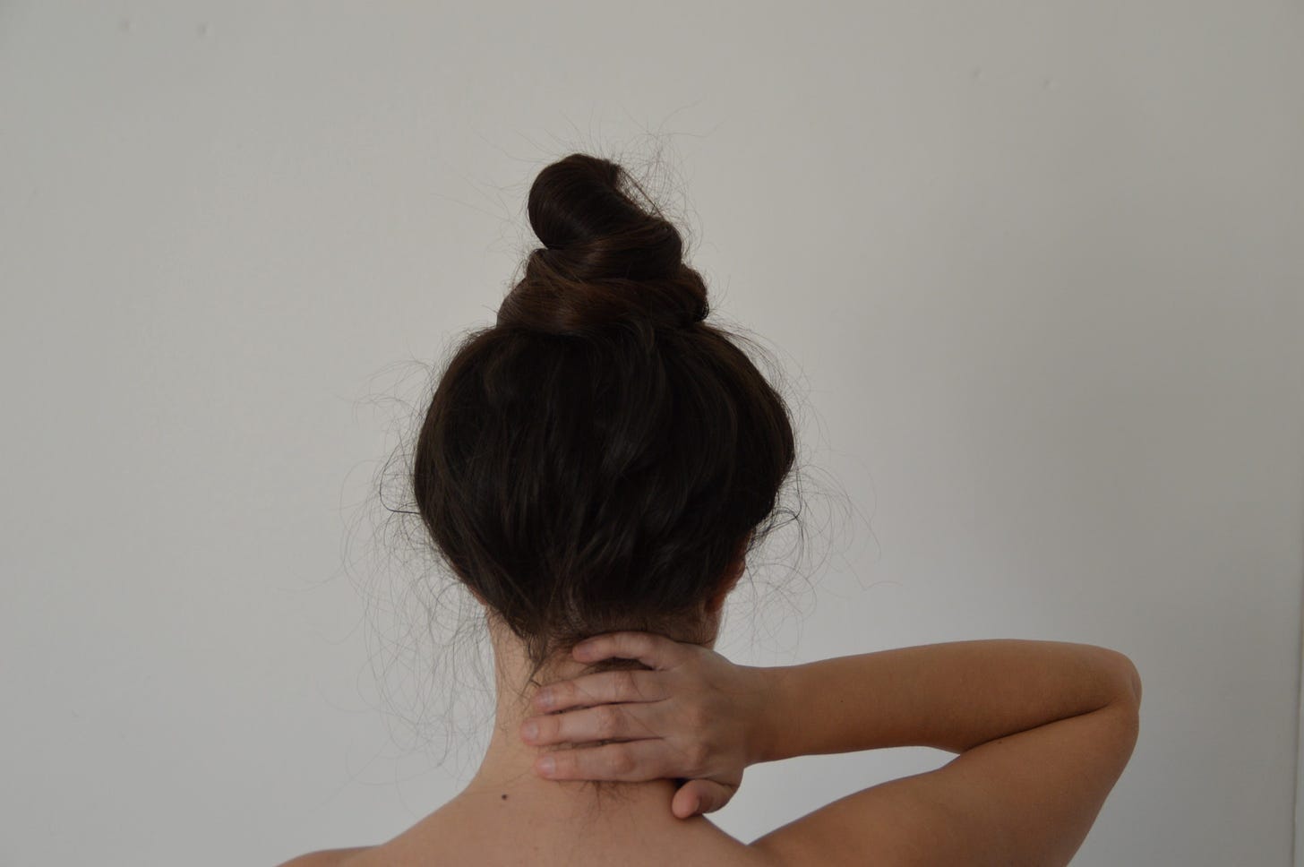 A woman with dark hair rubs her neck as she turns her back to the camera.