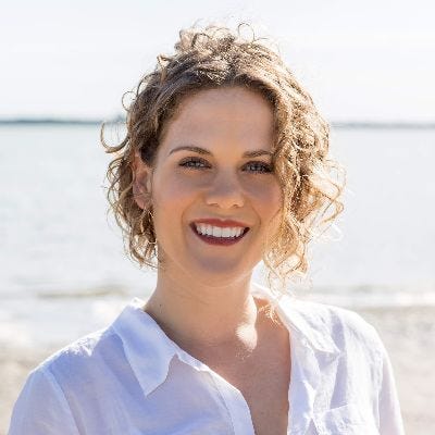 a white woman with shoulder length curly blonde hair smiling on a beach