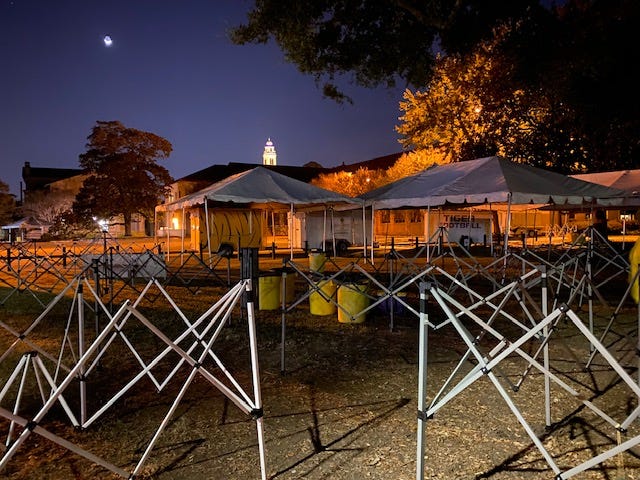 The campus of Louisiana State University is seen in the pre-dawn hours of Saturday morning, with a crescent moon hanging low. Tailgating tent frames are partially assembled in the foreground.