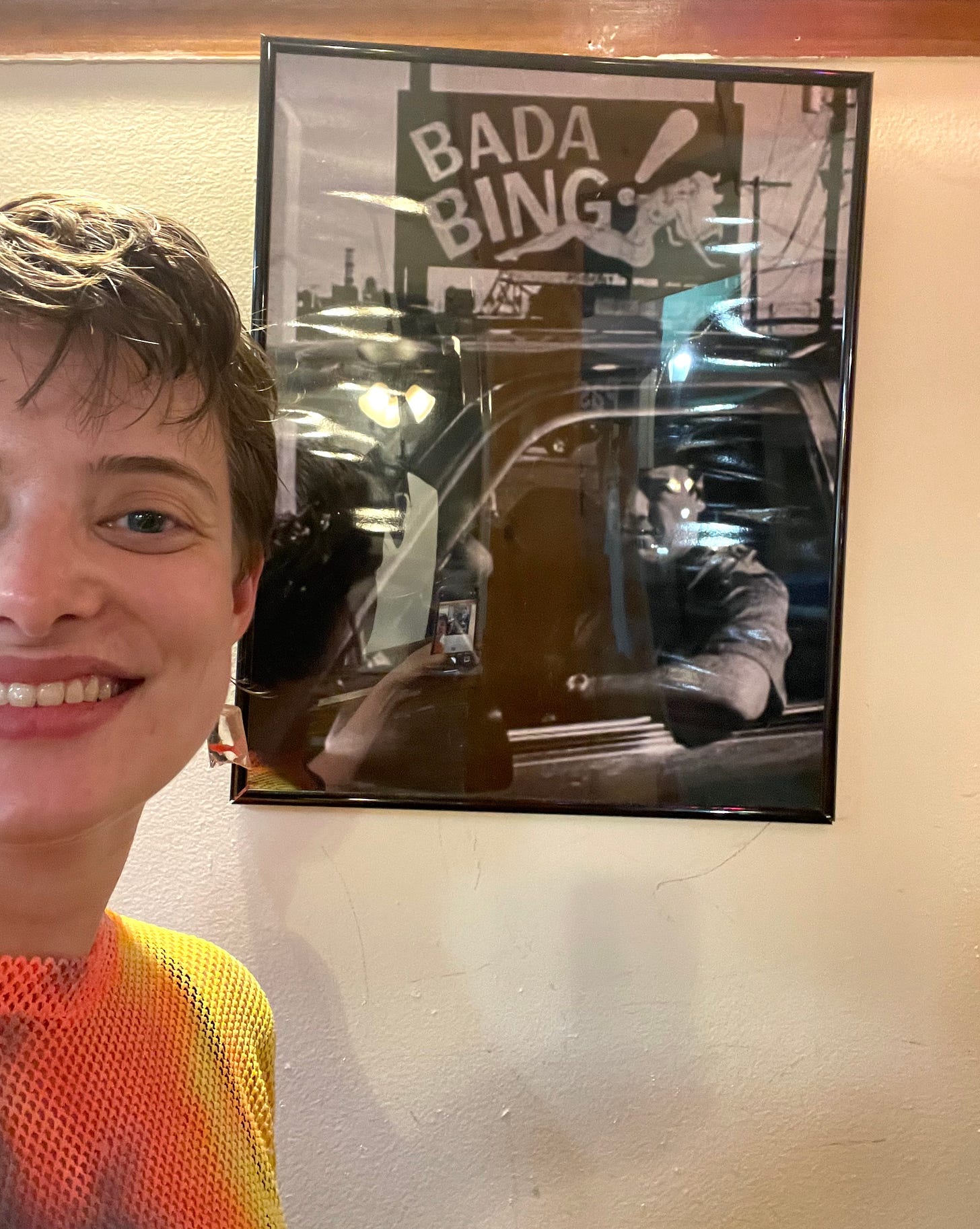 cassidy smiling in front of a framed photo of Tony Soprano in a car outside the Bada Bing