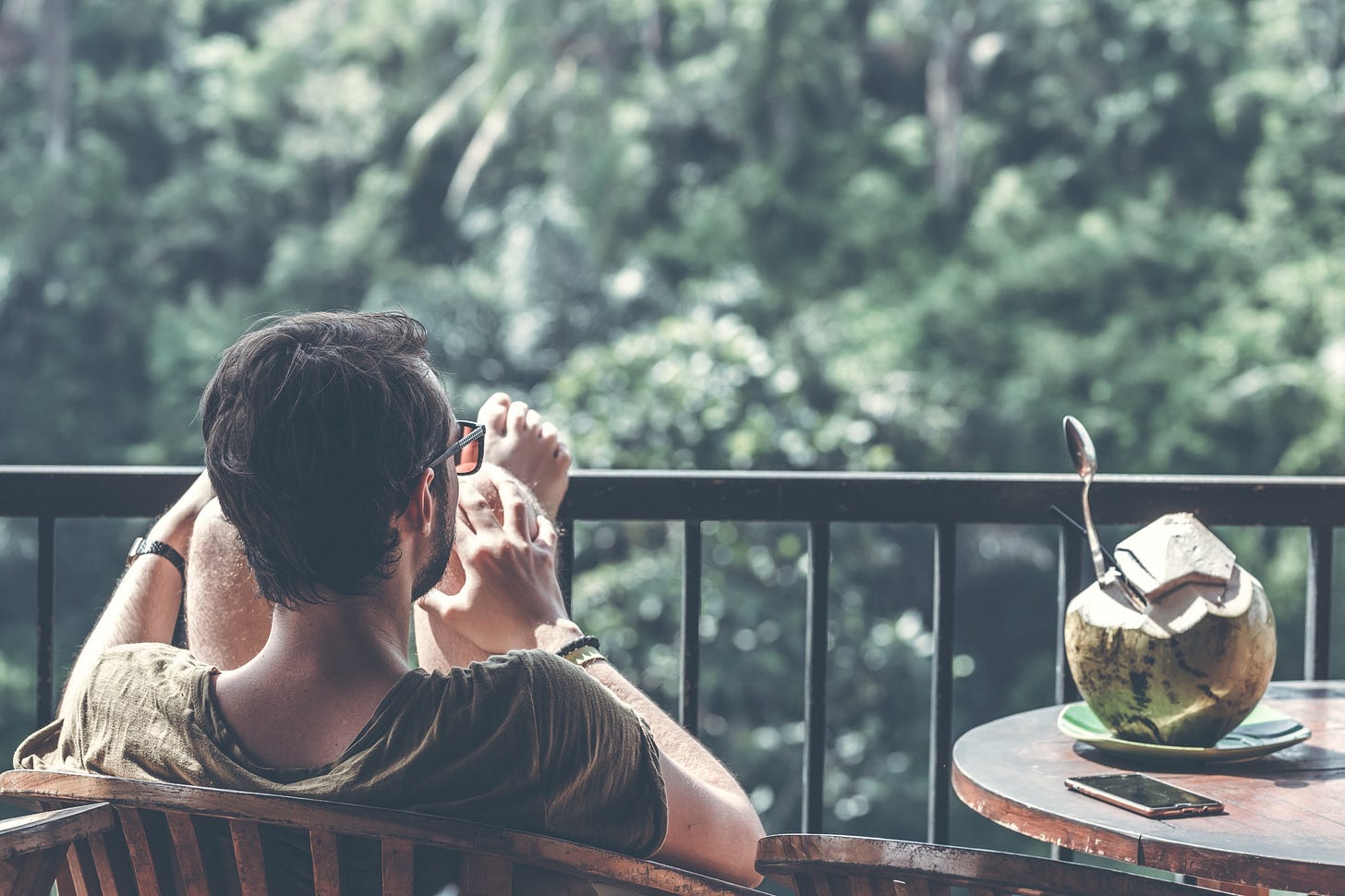 image of a man sitting in a chair on a balcony for article titled “In Support of The Idle Unambitious” by Larry G. Maguire