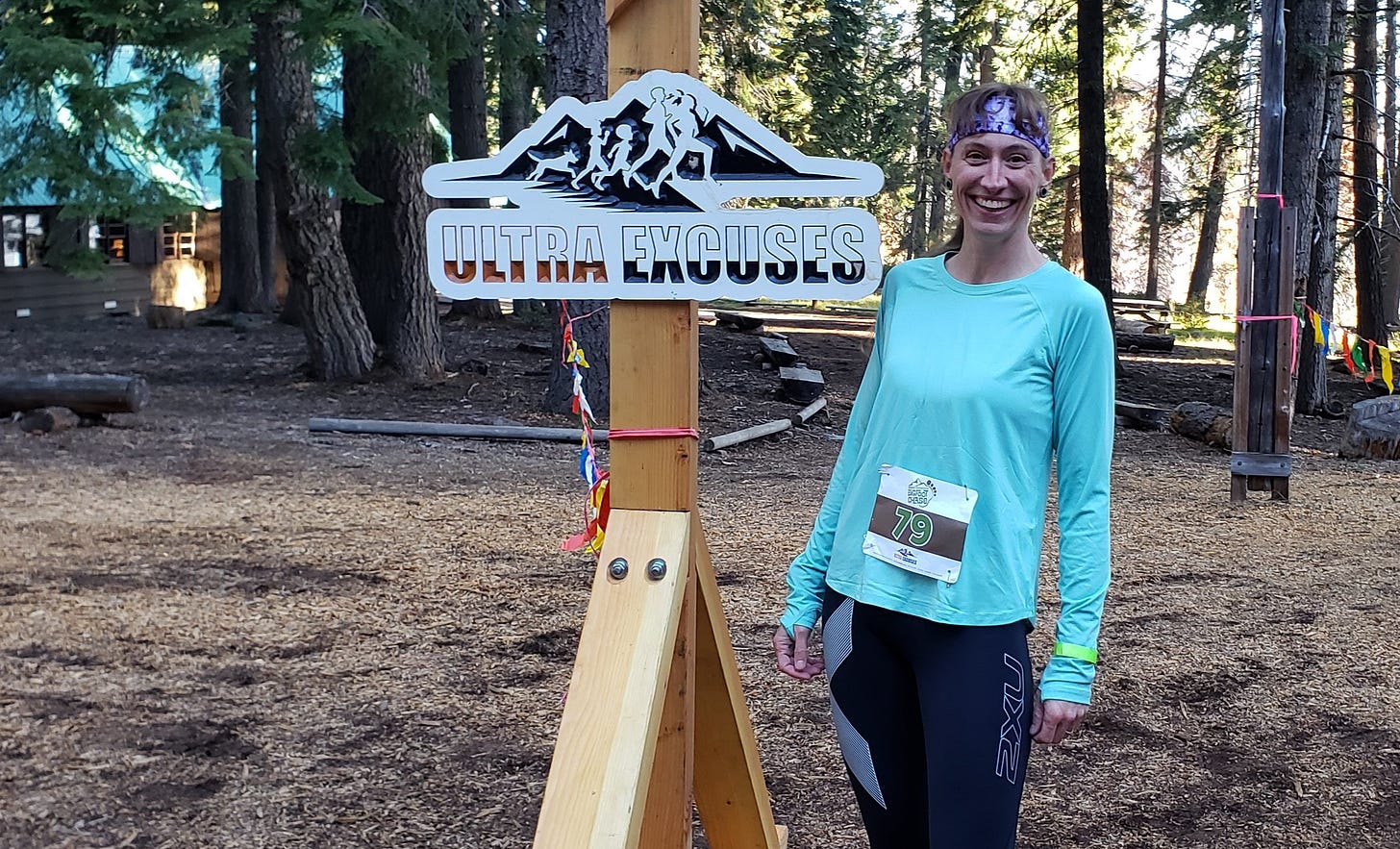 a woman in race gear standing at a finish line in the woods
