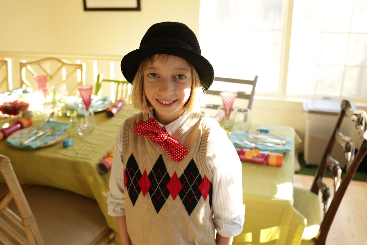Bea, a young girl smiling at the camera, wearing a fedora, sweater vest and bow tie. 