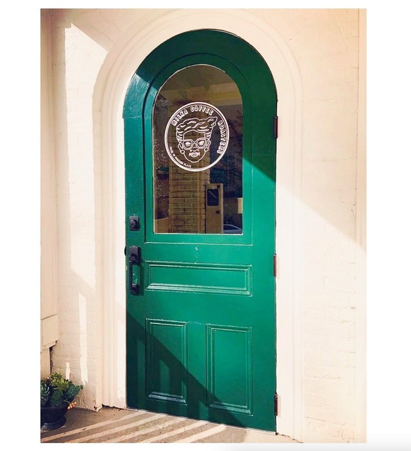 A close-up of an arched green door in a cream colored home.
