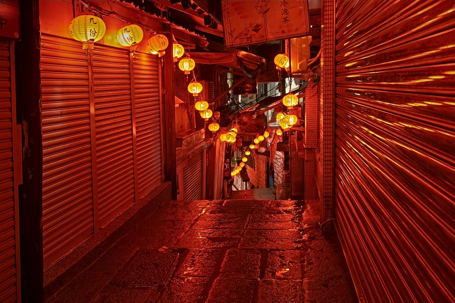The closed metal doors of shops along the narrow alleys of Jiufen Old Street 九份老街 reflect the light of red lanterns