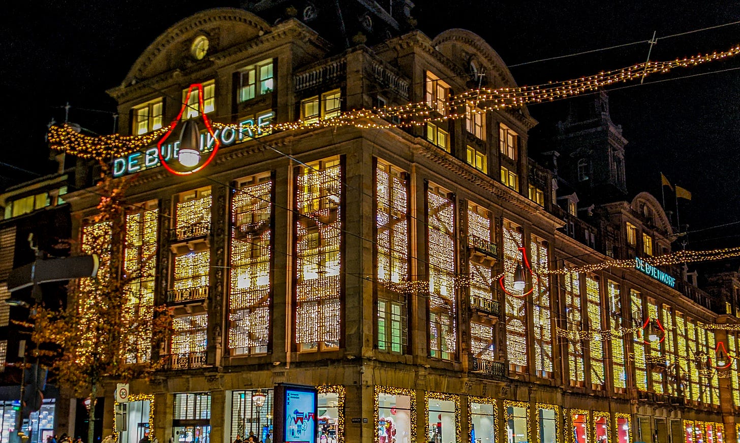 A Dutch department store with huge windows lit up with golden lights at night. 