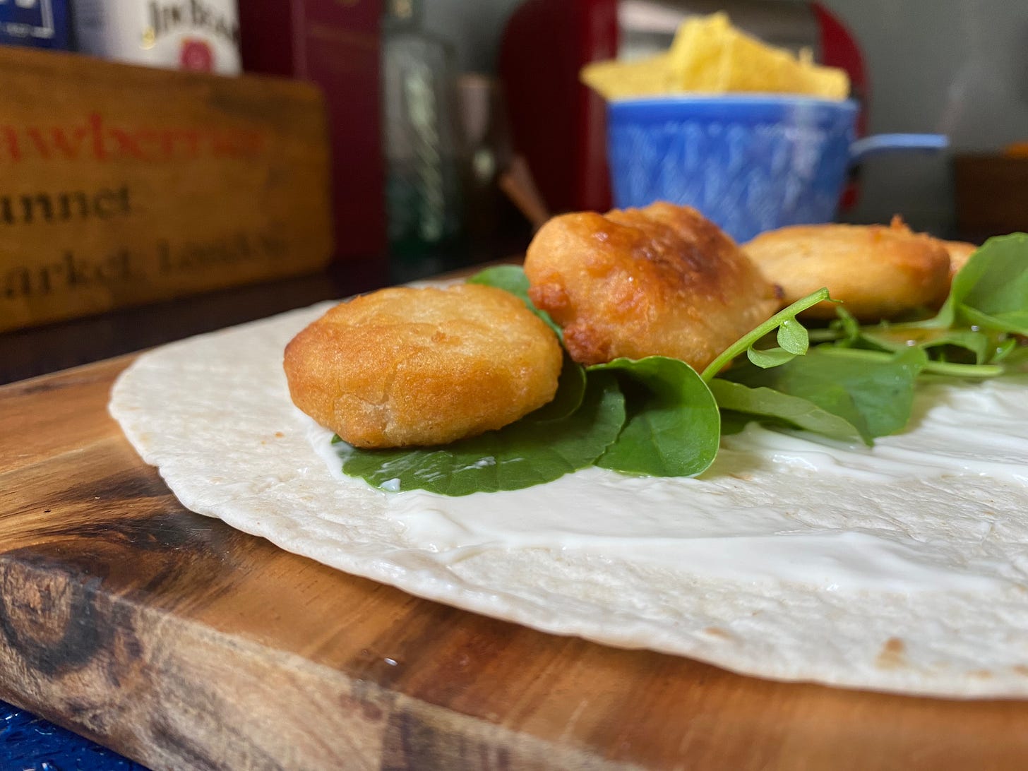 Wooden board with an open tortilla wrap with nuggets, mayonnaise and salad leaves