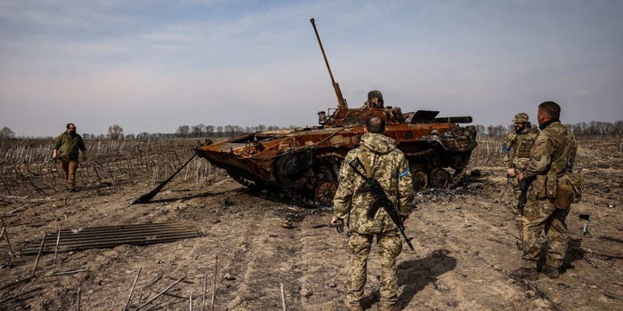 Ukrainian soldiers standing near a burnt Russian tank