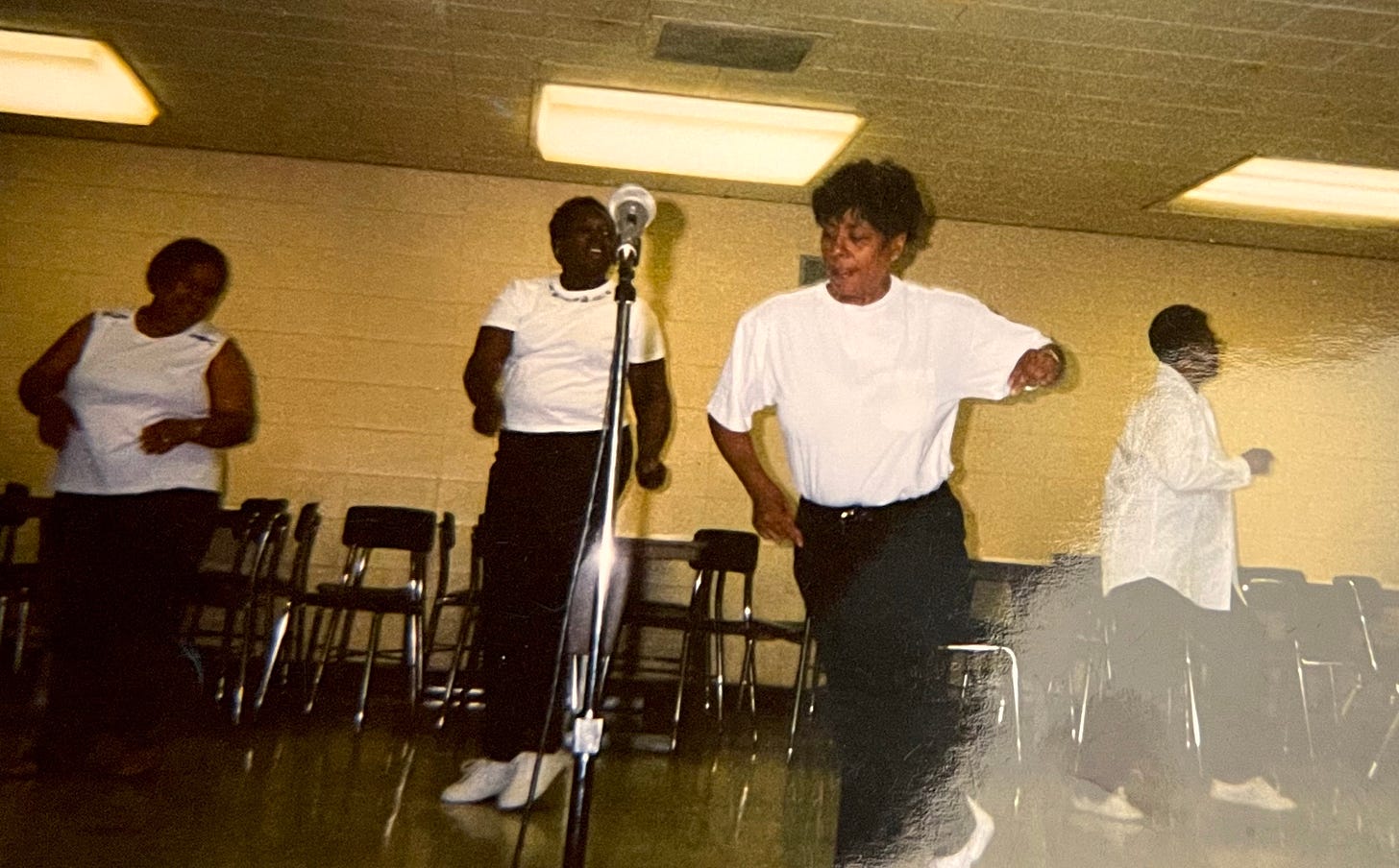 Jemar's mom dancing in black jeans and a white t-shirt along with three other women in the background