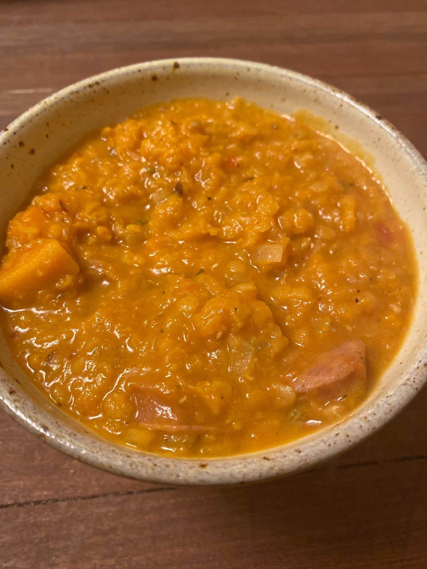 A ceramic bowl of red lentil stew, with chunks of butternut squash and pieces of sausage.
